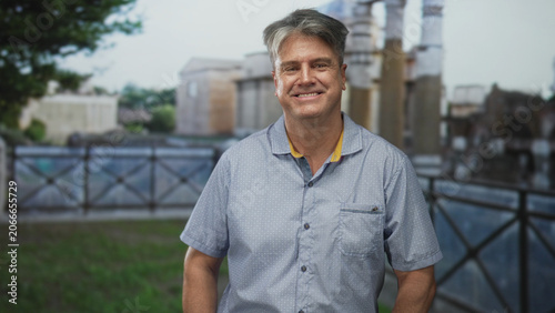 Fotografía Man smiling at camera by an old building with columns and railing, wearing a collared shirt and shortsleeve; nostalgic contentment