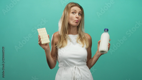 Canvas Print Woman holds white chocolate bar and glass milk bottle while puckering lips in a studio with teal backdrop and soft lighting; playful indecision