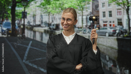 Photos Woman judge holding gavel aloft and smiling while standing on a street canal; justice authority confidence