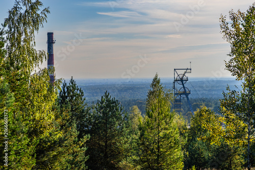 The steel shaft tower and chimney of the abandoned Boże Dary mine, surrounded by trees. View from the Kostuchna slag heap. Katowice, Silesia, Poland