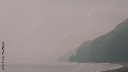 Misty Quiet Sandy Beach with a Rocky Silhouette in the Distance