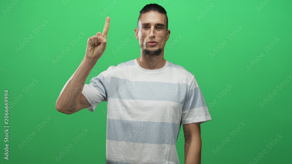 Fototapeta premium Man in striped t shirt holding up two fingers peace sign with right hand against green screen studio backdrop while making counting gestures; playful gesture.