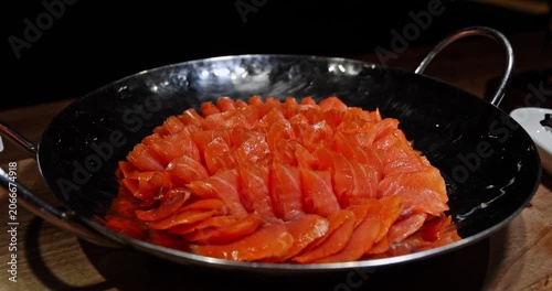 Sliced smoked salmon arranged in a hammered metal bowl on a wooden table at a restaurant buffet. Close-up shot of fresh seafood appetizer during dinner service. Nobody present.