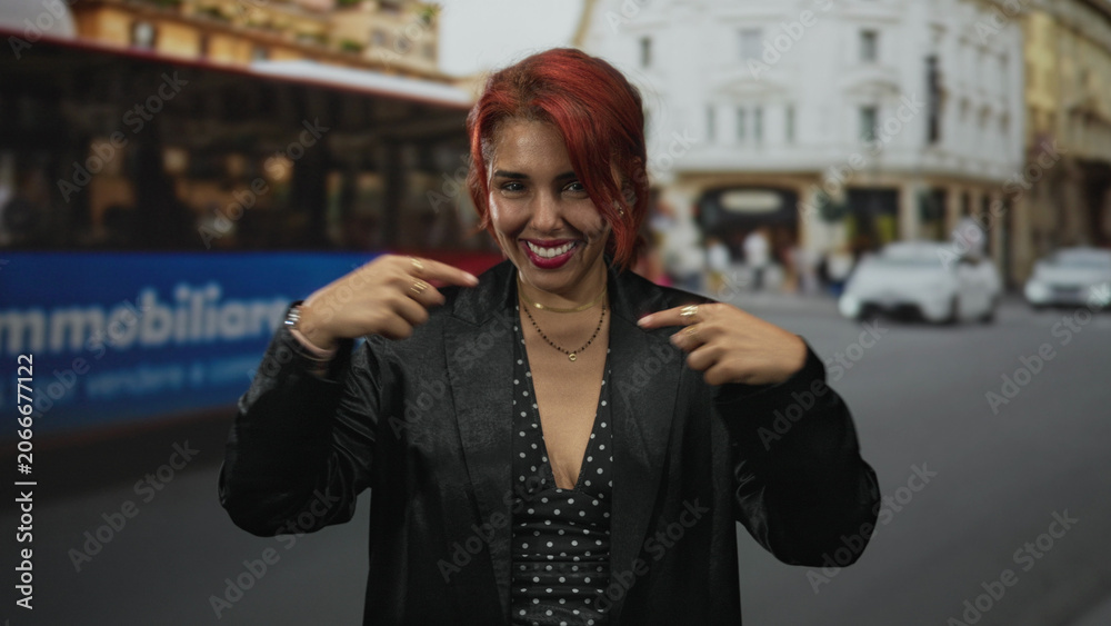 Fototapeta premium Woman points finger to chest on a busy city street near a red bus, smiling warmly; self confidence empowerment.