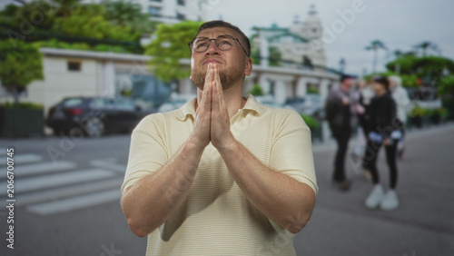 Fotografie Man with hands pressed together praying and looking upward on a busy city street amid blurred pedestrians; hope faith pleading
