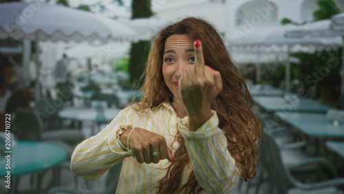 Foto Woman showing middle finger with red nail at restaurant terrace outdoors, smiling and pointing hand toward camera; defiance