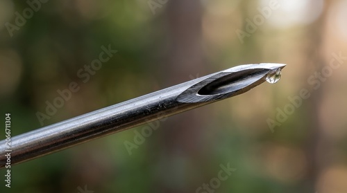 Close-up of metal needle tip with water droplet, blurred green background