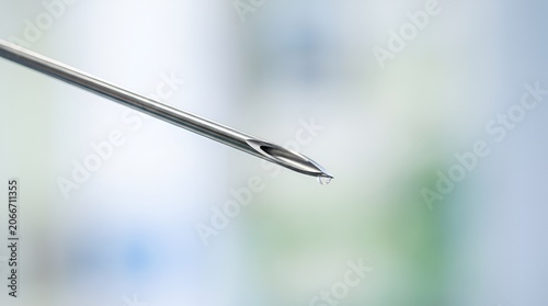 Close-up of sterile medical syringe needle with liquid drop, macro photography.