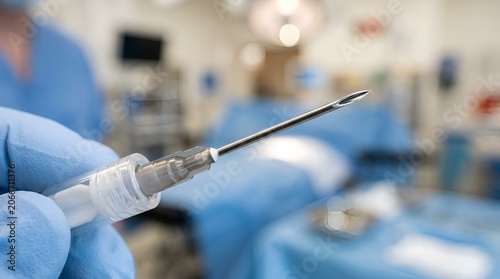 Close-up of sterile syringe needle held by gloved hand in surgery room