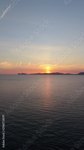 Aerial push-in view of Capo Caccia at sunset showing dramatic limestone cliffs and Mediterranean sea in warm golden hour light.