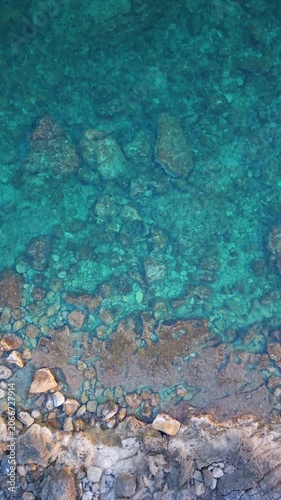 Top down view of clear water on a rocky shore in Sardinia showing submerged rocks turquoise sea and gentle wave movement in Mediterranean coastal environment.
