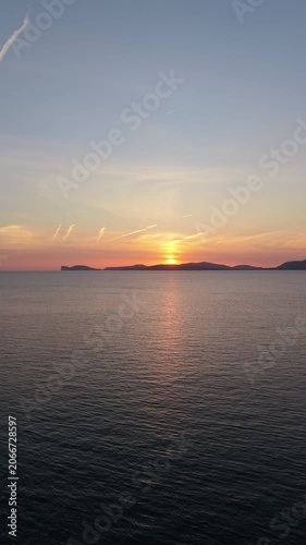 Vertical aerial view of Capo Caccia at sunset showing dramatic cliffs turquoise Mediterranean sea and golden hour light over the coastline.