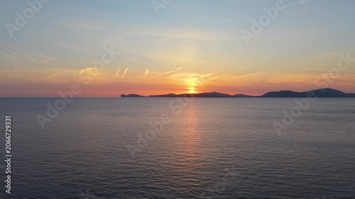Aerial fixed slow motion view of Capo Caccia at sunset showing dramatic limestone cliffs and Mediterranean sea in warm golden evening light.