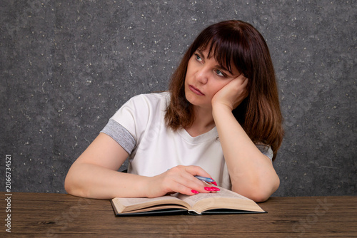 Tired middle-aged woman studying, boring reading a book in the evening