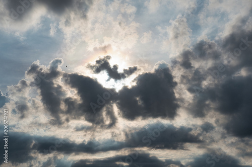 Bild auf Leinwand Dark thick clouds that partially obscure the bright sun twilight rays sunlight penetrating through clouds stormy weather or afternoon skies