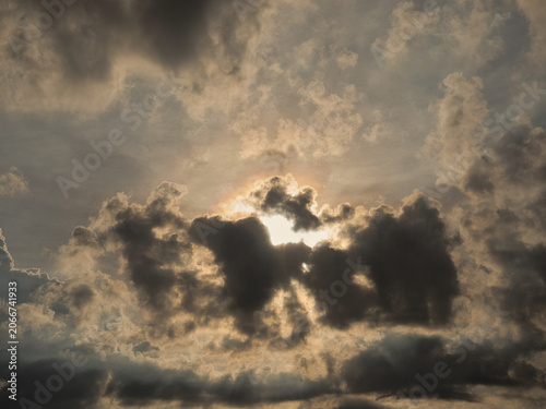 Billede på lærred Dark thick clouds that partially obscure the bright sun twilight rays sunlight penetrating through clouds stormy weather or afternoon skies