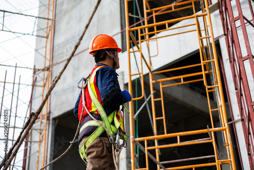 Construction worker wearing a safety harness while working on scaffolding at a building site.