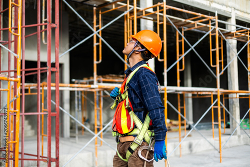 Construction worker wearing a safety harness while working on scaffolding at a building site.