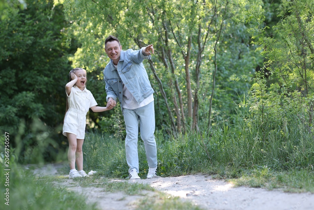 Fototapeta premium Smiling father pointing at something to his surprised daughter outdoors. Space for text