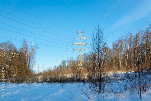 High voltage power lines and towers stretching across a snowy winter landscape with forest. Electricity transmission and power grid infrastructure.