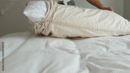 Hands removing white pillow from striped pillowcase on bed with white linens, domestic chore, laundry day, home maintenance, lifestyle .