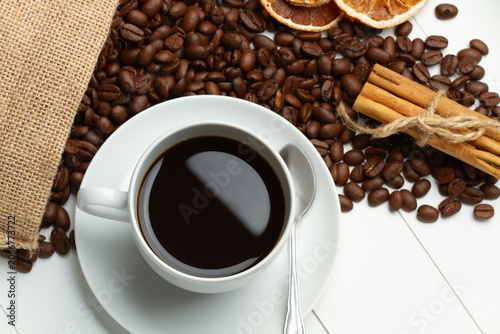 Una taza de cafe negro junto a granos de cafe y unas ramas de canela sobre un fondo blanco. Vista superior y de cerca