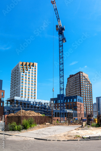 A construction site with tall buildings and a crane against a blue sky