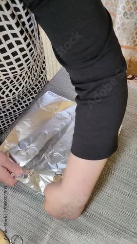 Woman's hands wrapping marinated pork meat with spices in aluminum foil for baking, Preparing homemade roasted meat roll with seasoning on the table close-up.