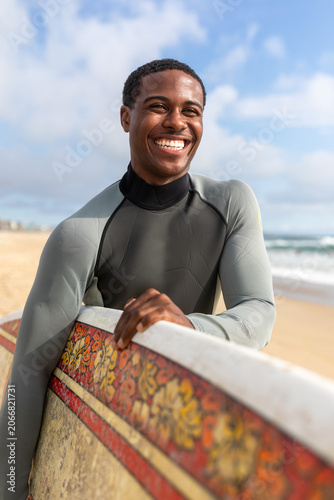 Konstfotografi Smiling surfer holding surfboard beachside