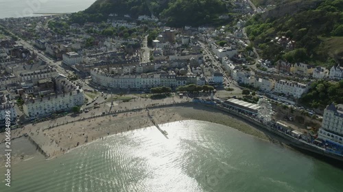 This aerial view shows the busy beach in Llandudno, North Wales during a sunny day. People are relaxing on the sand and enjoying various activities along the coastline