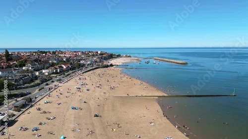 People are relaxing on the sand and swimming in the sea at Colwyn Bay Beach. Boats are visible in the water while the sun shines on a clear day