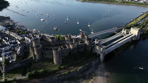 Witness Conwy Castle from above as it stands proudly beside the water. The surrounding area includes boats and a bridge, showcasing the historical site and its landscape in detail
