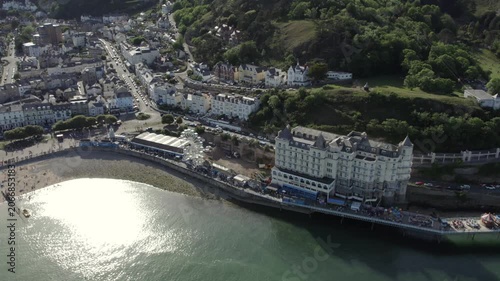 Aerial views capture a hotel located by the coast in Llandudno, North Wales. The footage shows the beach, pier, and nearby town. Enjoy the landscape and coastal details