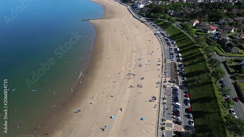 An aerial perspective of Colwyn Bay Beach in the UK, highlighting visitors enjoying the sand and the nearby cars parked along the road
