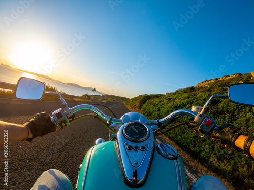 A biker rides a motorcycle along a coastal road at sunset