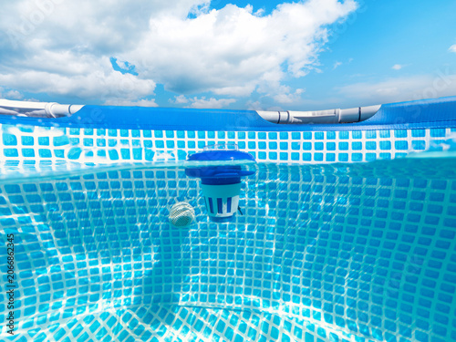 Split Underwater View of Chlorine Dispenser Floating in Swimming Pool Under Cloudy Sky