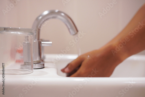 Chrome faucet with flowing water in a bathroom sink, showcasing hands cleaning for hygiene, skin health. Suitable for personal care concepts.