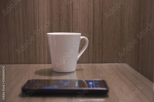 White ceramic coffee mug, black smartphone on a smooth wooden table, perfect for minimalist lifestyle blog headers and social media posts.