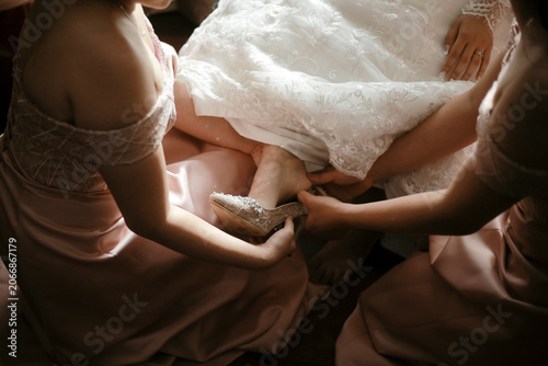 Foto Bridesmaids in elegant pink dresses helping the bride put on her beautiful lace crystal shoes
