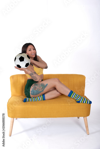 Young woman sitting on sofa holding a soccer ball in a creative studio portrait