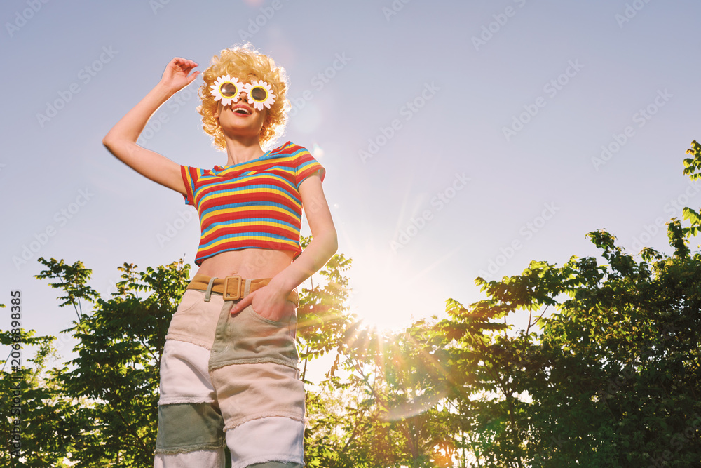 Obraz premium Woman lifestyle portrait with retro film color in sunny outdoors, a playful fashion scene, striped top and shorts under bright sunlight, smiling carefree in garden.