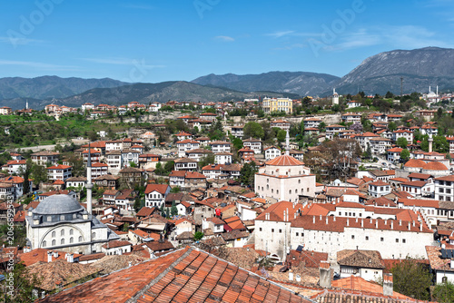 Aerial panoramic view of Safranbolu old town with historic Ottoman houses, mosques and mountains under blue sky.