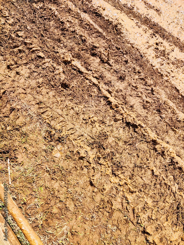 Muddy off-road track at an outbound adventure area, marked by tire ruts from vehicles and motorcycles, showcasing challenging terrain conditions and outdoor recreational activities on a sunny day.