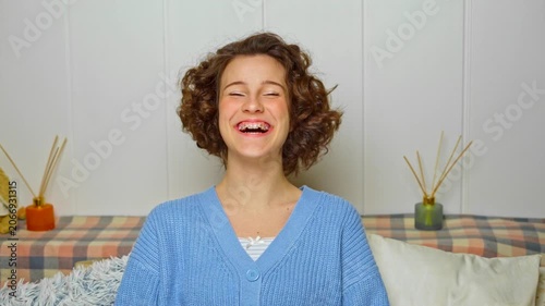 authentic moment of a joyful young woman with curly hair and braces laughing candidly, radiating happiness and positive emotions in a cozy home setting
