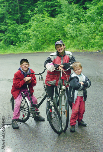 Authentic early 2000s children in oversized sportswear with bicycle outdoors