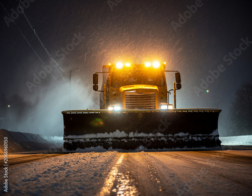 Giant highway snow plow truck with lights flashing during a snowstorm at night