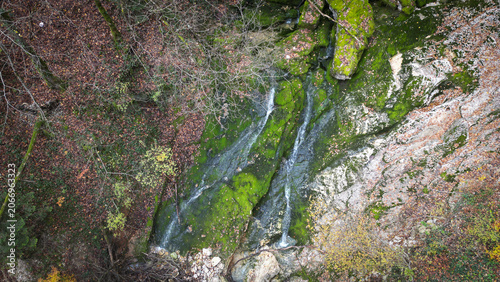 Aerial view of La Source de l'Allondon featuring a cascading stream flowing over mossy rocks surrounded by autumn foliage in Echenevex, Auvergne-Rhone-Alpes, France.