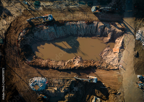 An aerial perspective shows a large excavation site where hydraulic excavators are removing soil to prepare the ground for future construction.