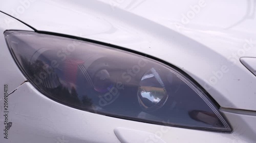 Wash the headlights of a car. A person washes the car's headlights with a sponge.