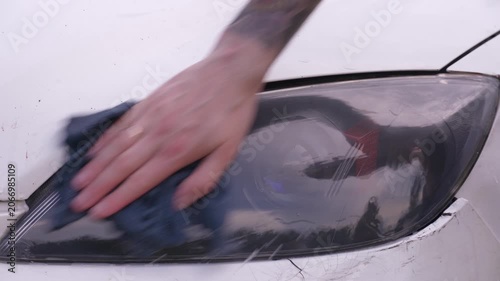 Wash the headlights of a car. A person washes the car's headlights with a sponge.